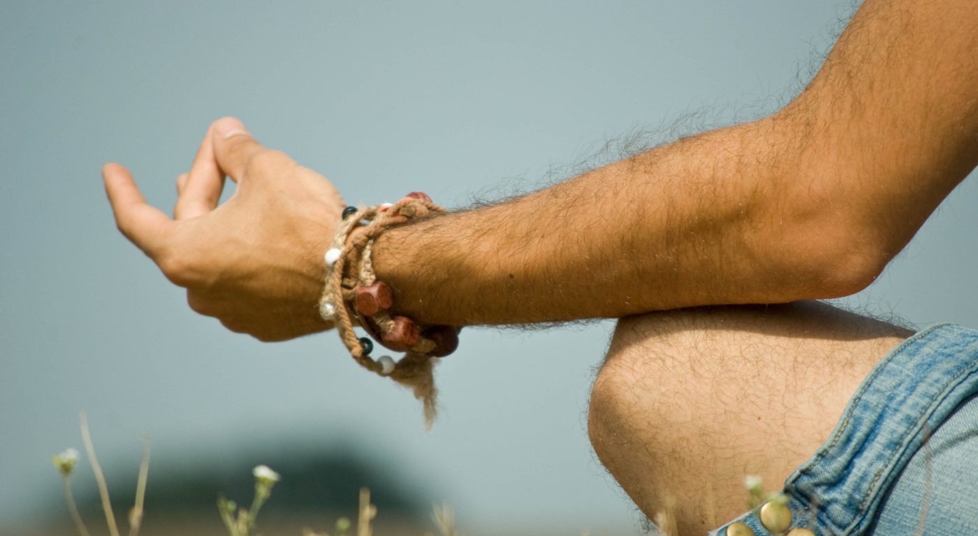 Close up of man's hand resting on her knee with fingers in meditation pose.